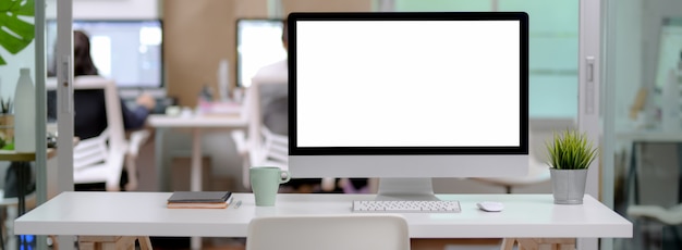 Photo close up view of office desk with blank screen computer, mug and notebooks in glass partition office