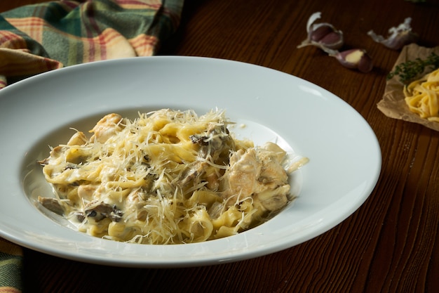 Close up view Pasta with wild mushrooms, white sauce, Parmesan cheese in white bowl on wooden background.