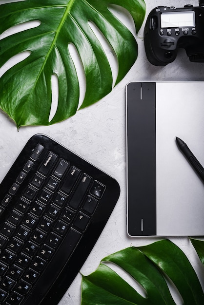 Close-up view of photographer's of graphic designer's
workplace. tablet, stylus, camera, keyboard with russian and
english letters, monstera green leaf.