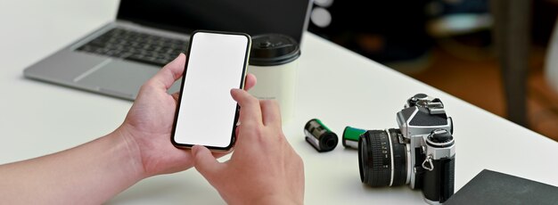 Chiuda sulla vista del fotografo che utilizza lo smartphone dello schermo in bianco all'area di lavoro