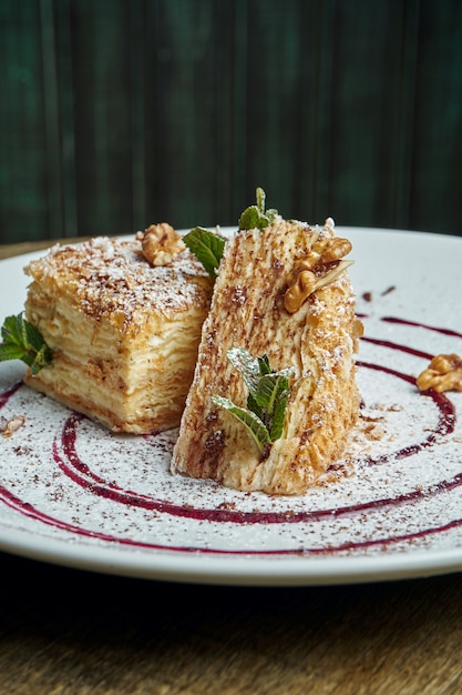 Close up view on piece of cake Napoleon with strawberry on ceramic plate on wooden surface. Russian cuisine, multi layered cake with pastry cream. Selective focus