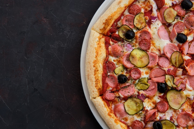 Close up view of pizza with defferent kind of sausages, pickled cucumber, olives and onion