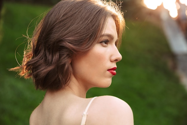 Close up view of pretty woman in dress looking away while posing outdoors