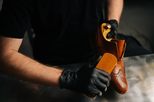 Vista ravvicinata di un calzolaio professionista in guanti neri che lucida scarpe in pelle marrone chiaro con una spazzola durante i lavori di restauro. concetto di manutenzione delle calzature catturato.