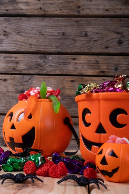 Close up view of pumpkin shaped bucket full of halloween candies and toys on wooden surface. halloween festivity and celebration concept