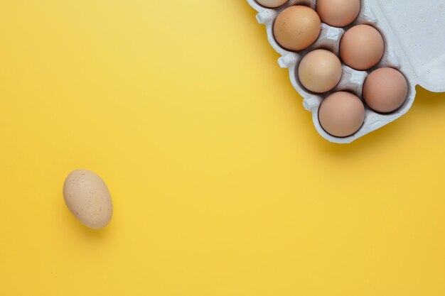 Close-up view of raw chicken eggs in egg box on yellow background