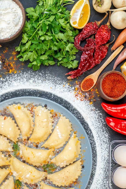 Close up view of raw dumplings on blue tray with flour around and various foods on dark color surface