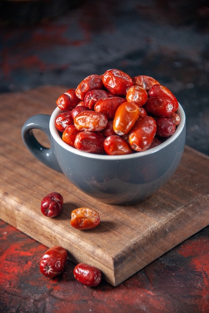 Close up view of raw silverberry fruits inside and outside of a gray color cup on wooden board on mix colors background