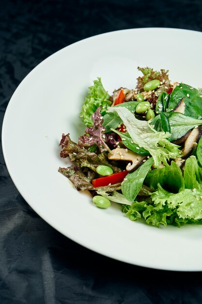 ほうれん草、マッシュルーム、ピーマン、若い豆、エンドウ豆のサラダを黒いテーブルの上の白いボウルにクローズアップ表示します。健康でダイエット食品。ベジタリアン