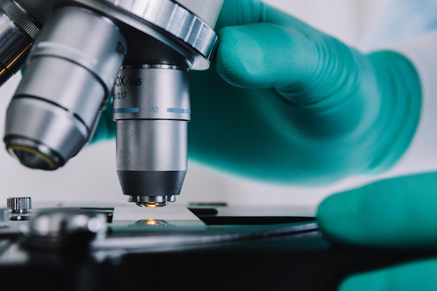 Close up view of scientist hands with gloves set the sample in the microscope for research