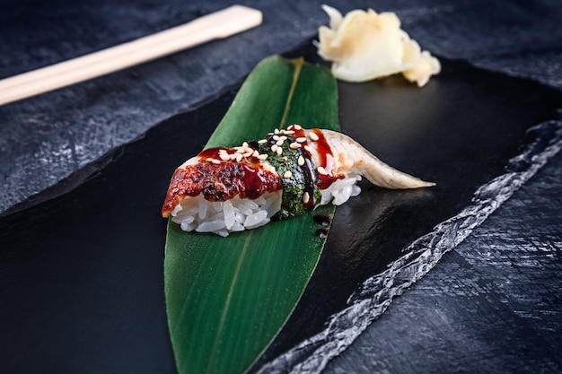 Close up view on served Nigiri with eel on dark plate on dark surface