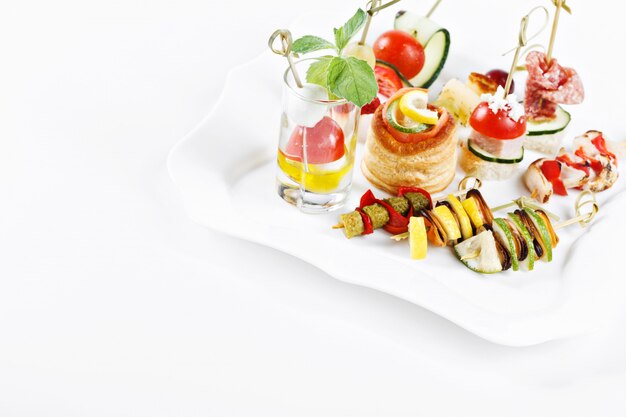 Close-up view set of canapes with vegetables, salami, seafood, meat and decoration on whie plate studio isolated