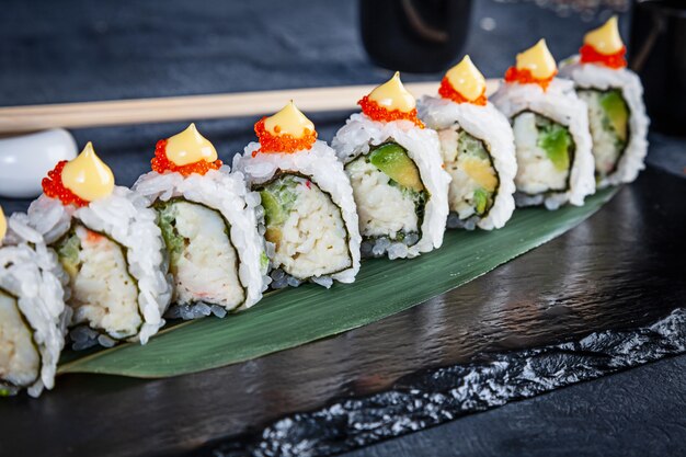 Close up view on set of sushi roll. California roll with crab, avocado and caviar served on black stone on dark background. Japanese cuisine. Copy space. Served sushi for menu. Healthy food, seafood