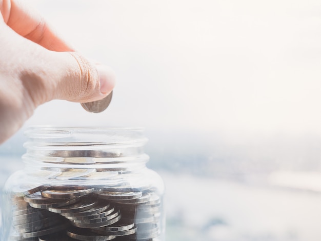 Photo close up view on the side of the hand holding a coin to put money in a glass bottle