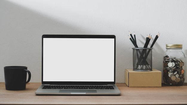 Close up view of simple workspace with blank screen laptop, coffee cup and stationery