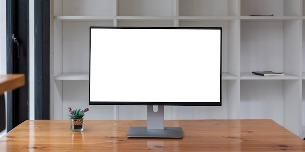 Close up view of simple workspace with open blank screen laptop, frame and notebook on white table with blurred office room background