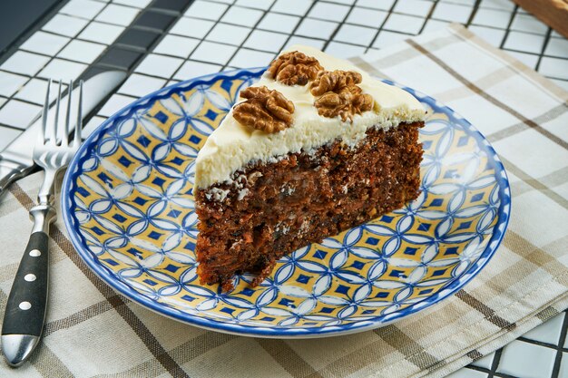 Close up view on Slice of carrot cake with cream and nuts on a blue ceramic plate on a white table. Healthy dessert.