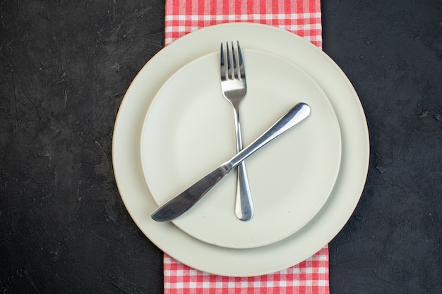 Close up view of stainless cutlery set on white empty plates on red stripped towel on black background with free space