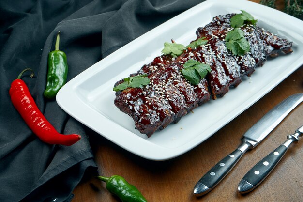 Close up view on tasty delicious bbq cooked ribs with barbecue sauce in white plate on wooden table. Classical american Barbecued Pork in composition with ingredients