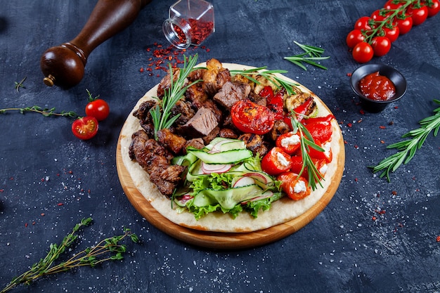 Close up view on tasty grilled meat with vegetables on georgian pita. shashlik or barbecue meat on pita. shish kebab, traditional georgian cuisine food. copy space for design. dark background