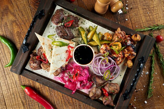 Close up view on tasty grilled meat with vegetables on georgian pita. shashlik or barbecue meat on pita. Shish kebab, traditional georgian cuisine food. Copy space for design. Wooden surface