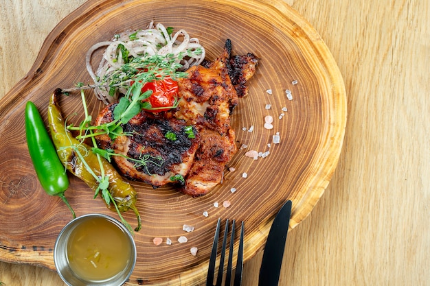 Photo close up view on tasty grilled steak from chicken on wooden board. composition with cooked beef, herbs and vegetables. food photo wall. selective focus. shashlik, kebab