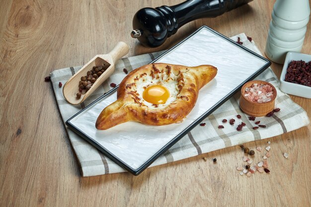 Close up view on tasty traditional Adjarian Khachapuri - open baked pie with melted salt cheese (suluguni) and egg yolk on wooden board. Traditional georgian food
