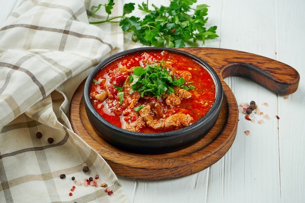 흰색 나무 배경에 갈색 세라믹 접시에 토마토에 조림 맛있는, 전통 Chashushuli-향기로운, 매운 고기 요리 (쇠고기 또는 송아지 고기) 에보기를 닫습니다