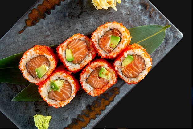 Close up view on tasty uramaki with salmon, avocado and tobiko caviar. Japanese traditional cuisine. Food delivery. Isolated on black