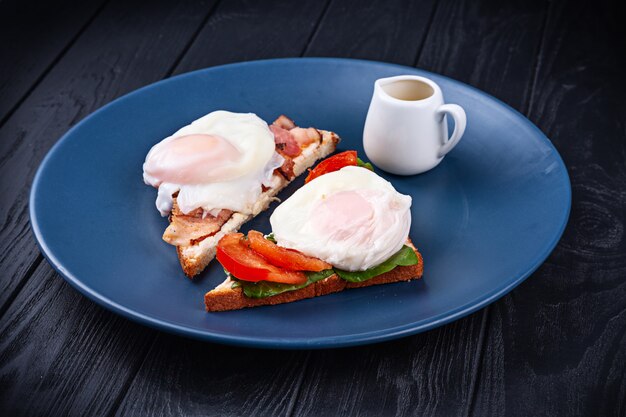 Close up view on toast with poached egg, bacon melted cheese and spinach, tomato