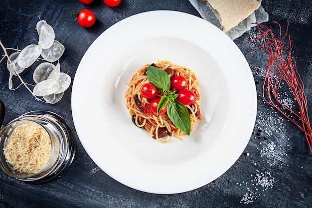 Chiuda sulla vista su pasta italiana tradizionale con basilico e pomodoro ciliegia in piatto bianco. piatti piatti della cucina italiana con copia spazio per il design. tagliatella mediterranea a pranzo. vista dall'alto