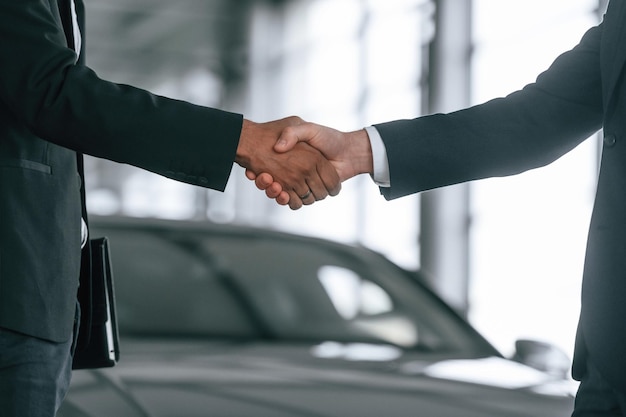 Close up view Two businessmen are standing in the car showroom and making a deal handshake