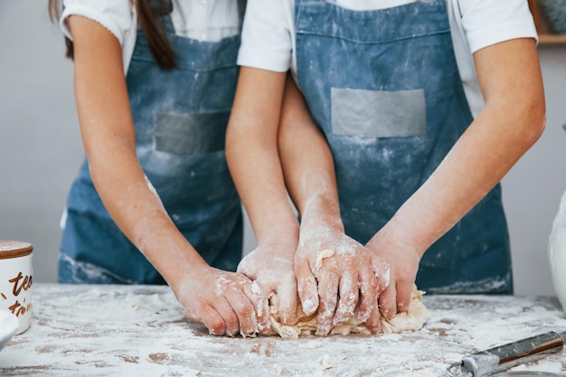 Foto vista ravvicinata di due bambine in uniforme blu da chef che preparano il cibo in cucina