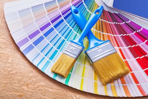 Close up view on two paint brushes with blue handles on color palette and wooden board