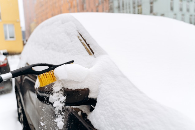 特別なブラシで雪から車を掃除している認識できない人のビューをクローズアップします。車のコンセプトから雪を掃除するための装置。ストックフォト