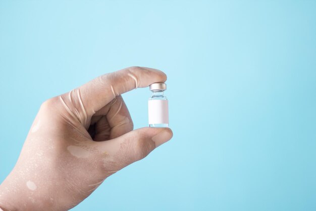 Close-up view of the vaccine and syringe in the doctors hand with a blue background