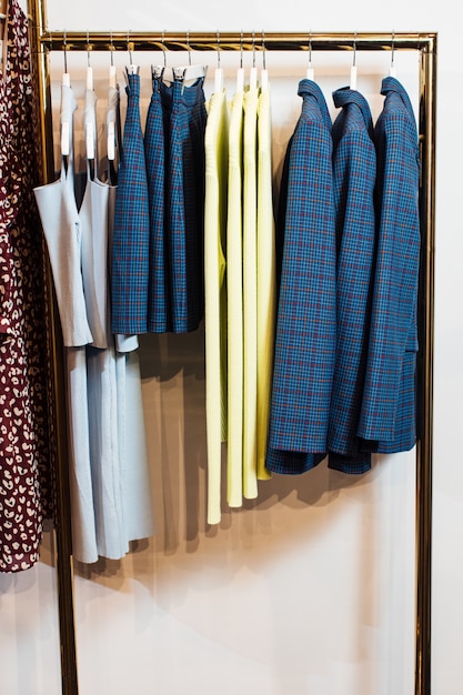 Close up view of various stylish clothes hanging on hangers in boutique