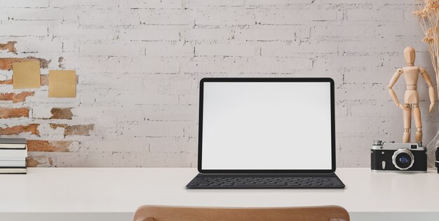 Close-up view of vintage workplace with blank screen tablet and office supplies on white desk and brick wall