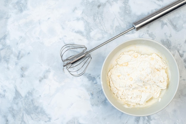 Close up view of white flour in a bowl and stainless cooking tool on the left side on two-toned background