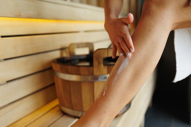 Close up view of woman applying moisturizer cream on leg skin in sauna