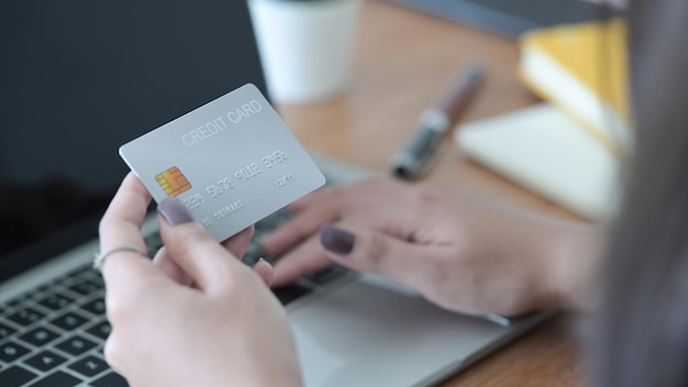 プラスチック製のクレジットカードを保持し、ラップトップを使用して女性の手をクローズアップビューオンラインショッピングインターネットバンキングの概念