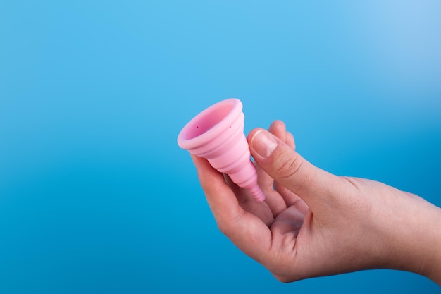 Close up view of woman holding pink menstrual cup over blue background woman's period menstrual