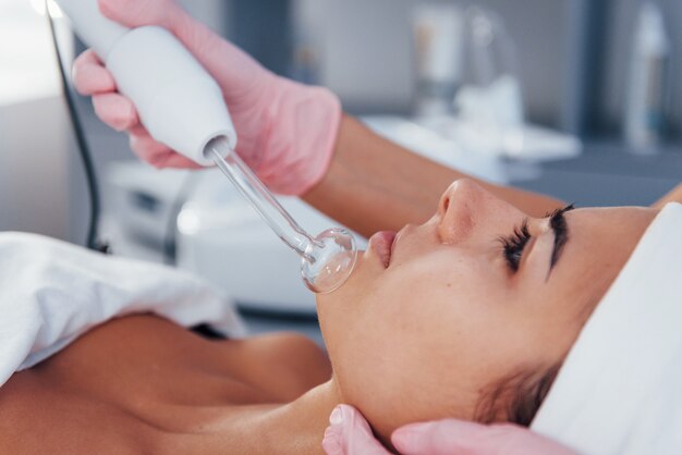 Close up view of woman that lying down in spa salon and have face cleaning procedure by using modern device.