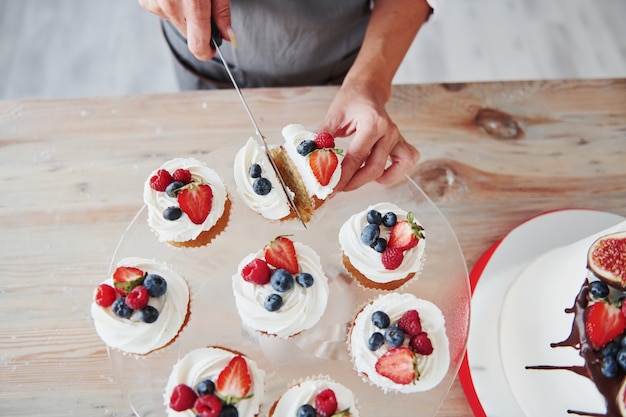 Close up view of woman that makes slices of the cookies by using knife in the kitchen with pie on the table.