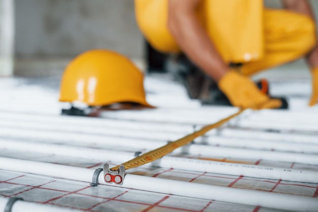 Close up view Worker in yellow colored uniform installing underfloor heating system