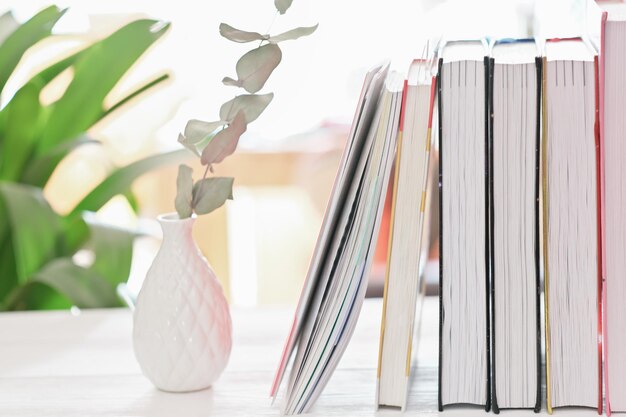 Close up view of workspace with books and ceramic vase on white desk learning and education cozy house working place