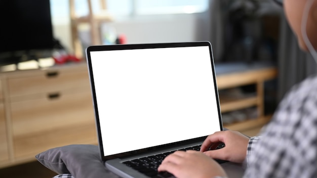 Close up view of young Asian girl sitting on comfortable sofa and using laptop computer.