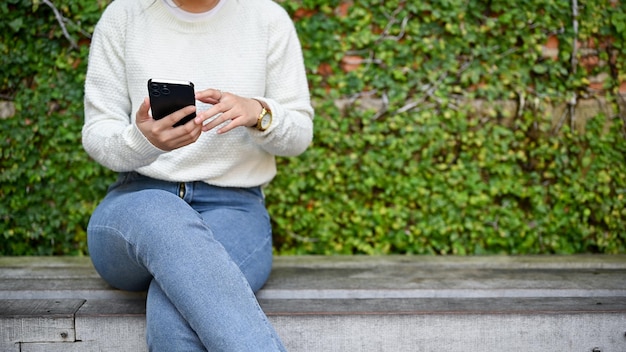 座っている間に公園でスマートフォンを使用している若い女性のクローズ アップ ビュー