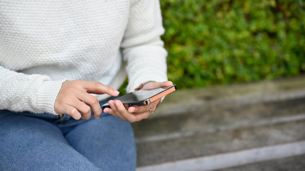 Close up view of young female using smartphone in the park while sitting