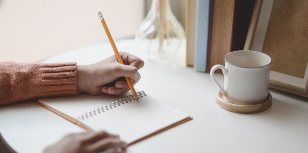 Photo close-up view of young female writing her idea on notebook while working on her project